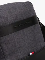 Bandolera Tommy Hilfiger modelo TH Melange Mini Reporter, color gris oscuro con detalles en negro. Presenta una franja horizontal con el logo de la marca y el detalle de la bandera en la parte inferior.