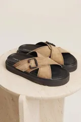 Sandalias planas color beige con tiras cruzadas y hebilla decorativa.