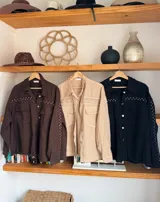 Chaqueta color beige con bordado calado, cuello camisero, cierre frontal con botones, mangas largas con puños abotonados, bolsillos de parche en el pecho y ruedo desflecado.