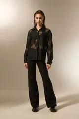 Camisa negra de poliamida con diseño calado de encaje floral, corte holgado, cuello camisero, botones frontales y mangas largas.