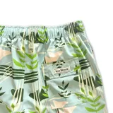 Short de baño celeste con estampado de hojas verdes y formas geométricas en blanco y negro. Tiene elástico en la cintura, cordón ajustable y tres bolsillos.