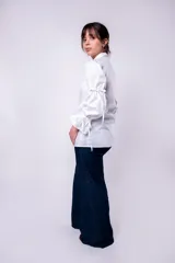 Camisa blanca de mangas largas abullonadas con lazos en los puños y cuello clásico. Cierre frontal con botones.