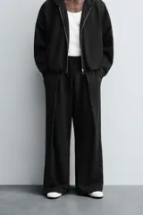 Pantalón jogger negro de corte relaxed fit, confeccionado en tejido de algodón. Presenta cintura elástica ajustable con cordón, pliegues frontales, bolsillos delanteros y un bolsillo trasero.