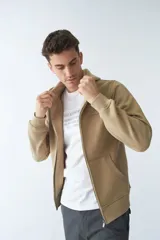 Campera de felpa color beige con cierre frontal, capucha con cordón ajustable, bolsillos laterales y logo estampado en el pecho.