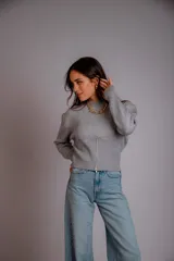 Buzo gris de punto con cuello redondo, mangas largas abullonadas y cierre frontal asimétrico.