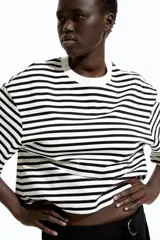 Remera cropped de algodón a rayas horizontales negras y blancas, de corte holgado con cuello redondo acanalado, hombros caídos y bajo recto.