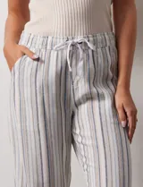 Pantalón de lino a rayas verticales grises y blancas, con pretina elastizada, lazo de ajuste y bolsillos delanteros y traseros.