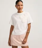 Blusa blanca de algodón con cuello redondo, mangas cortas y apliques florales en el hombro.