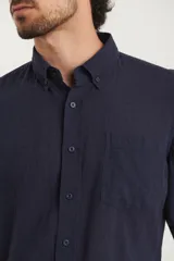 Camisa azul marino de lino y algodón, con cuello abotonado, manga larga con puños enrollados, bolsillo de parche en el pecho y cierre frontal con botones.