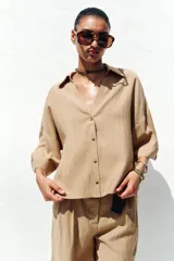 Camisa color beige de cuello solapa con escote pico y manga corta ancha acabada en vuelta con trabilla y botón. Cierre frontal con botones.