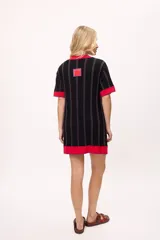 Vestido de tejido de punto, color negro con rayas verticales grises. Tiene cuello redondo y puños y ruedo en color rojo con costuras decorativas en hilo azul. Presenta un pequeño bordado de una letra 'B' estilizada en el pecho.