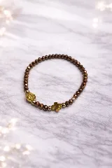 Pulsera elástica compuesta por cuentas facetadas de color marrón oscuro con acabado metálico, intercaladas con cuentas más pequeñas de color dorado. Incluye un dije de cruz dorada y un dije redondo con una medalla religiosa grabada en dorado.