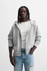 Sudadera gris con capucha, corte holgado, cierre frontal con cremallera, bolsillos laterales ocultos y terminaciones irregulares.