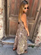 Vestido largo, con breteles finos y escote en V tanto adelante como atrás. Presenta un estampado de hojas en tonos marrón y beige sobre fondo rosado pálido.