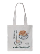 Bolso tote bag de tela color crudo con asas largas. Presenta un estampado gráfico de estilo café con ilustraciones de un croissant, una taza de cappuccino y una taza de espresso, junto con texto en inglés.