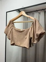 Top corto color marrón claro, con escote cuadrado, mangas cortas abullonadas con elástico y espalda fruncida.