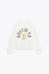 Sudadera blanca de algodón con cuello redondo y mangas largas. Estampado frontal con texto "Texas Rodeo 1995 United States" en color marrón.