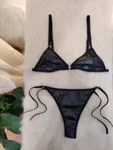 Conjunto de bikini negro de cuerina, con corpiño triangular y bombacha colaless con tiras laterales ajustables.