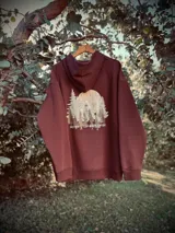 Buzo hoodie color marrón con estampa de paisaje de montaña y texto "Never Stop Exploring" en la espalda.