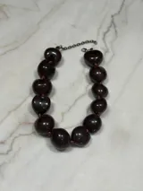 Collar corto de cuentas color marrón oscuro con forma de corazón, unidas por hilo marrón y cadena plateada con cierre de mosquetón.