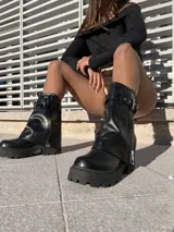 Botas negras de ecocuero con caña media, cartera con cierre y cinto decorativo.