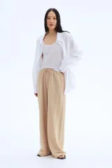 Pantalón de punto color beige, de corte holgado con piernas amplias, tiro alto, cintura elástica y cordón para ajustar.