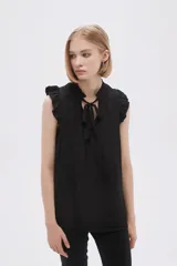 Blusa sin mangas color crudo con cuello con lazo y volados en los hombros.