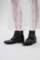 Botas cortas de cuero negro con tachas plateadas en la puntera y el talón, cierre lateral con cremallera y hebillas decorativas. Taco cuadrado bajo.