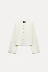 Chaqueta color crema de punto canalé con cuello redondo, manga larga y cierre frontal con botones marrones.