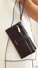 Billetera de mujer color negro, con textura símil cuero granulado. Presenta un cierre de presilla con broche, correa de mano desmontable y múltiples compartimentos internos, incluyendo un monedero con cierre.