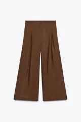 Pantalón cropped marrón de tiro medio y pierna ancha, confeccionado en hilatura con mezcla de lyocell. Presenta trabillas en la cintura, bolsillos laterales y pinzas en el delantero. Cierre frontal con cremallera y botón.