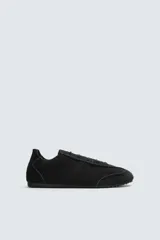 Zapatilla de cordones color negro, con capellada de cuero serraje, horma redonda y suela ultrafina.