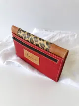 Billetera de cuero color rojo con solapa de cuero color marrón y aplique de cuero con estampado animal print.