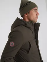 Parka verde militar de nylon con forro capitoneado color naranja, capucha con piel sintética desmontable, relleno de guata, bolsillos en pecho y bajos con cierre y parche personalizado en manga.