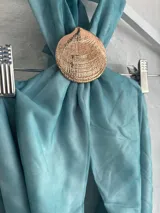 Top halter de color celeste/turquesa, con efecto drapeado y un accesorio tipo concha marina como broche central. El diseño es holgado y se ajusta en la espalda.