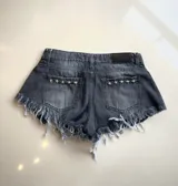Short de jean negro con efecto desgastado, tiro alto, corte ajustado, ruedo desflecado y apliques de estrellas metálicas en los bolsillos traseros.