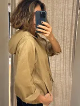 Chaqueta color beige de lino, con capucha, cierre frontal con cremallera negra, bolsillos laterales y mangas 3/4.