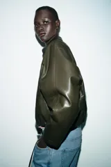 Chaqueta estilo bomber de efecto piel en color verde oliva, con cuello solapa, cierre frontal con cremallera, mangas largas y bajo con acabado elástico.