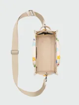 Bolso tote pequeño de lona color crema con estampado de margaritas de colores, doble asa superior y correa bandolera ajustable y extraíble.