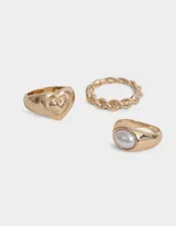 Set de tres anillos dorados con diferentes diseños: uno con forma de soga trenzada, otro con una perla y otro con un corazón.