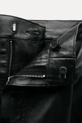 Pantalón de cuero negro de tiro medio, con pinzas delanteras, bolsillos laterales ocultos y corte holgado.