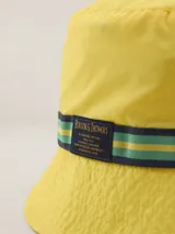 Gorro tipo bucket color mostaza con cinta decorativa a rayas horizontales en tonos bordó, amarillo y azul marino.