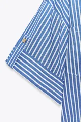 Camisa cropped de viscosa y lino a rayas verticales azules y blancas. Tiene cuello solapa, escote pico, manga corta con vuelta y bolsillos de plastrón.