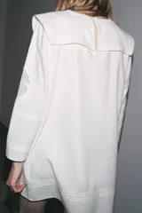 Vestido corto de algodón y lino color blanco, con cuello babero cuadrado, manga larga y bordados florales. Cierre en la espalda con abertura y botón.