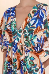 Vestido corto de manga mariposa, escote en V y cintura ajustada con frunce. Presenta un estampado botánico vibrante sobre fondo blanco, con hojas en tonos azules, naranjas y verdes.