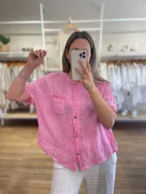 Camisa de lino y algodón color crudo, de corte recto, manga corta y cuello redondo con abertura frontal con botones. Tiene un bolsillo en el pecho con detalle de puntilla.