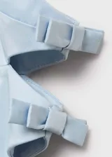 Vestido corto celeste con breteles finos, escote recto, corte ajustado, aberturas laterales y lazos decorativos en los laterales. Cierre con cremallera en la parte posterior.