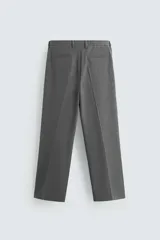 Pantalón negro de corte ancho con cintura elástica, pliegues frontales, bolsillos laterales y traseros de vivo. Tiene detalle de hebilla metálica en la trabilla y cierre frontal con cremallera y botón.