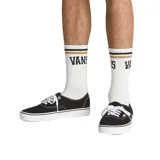 Medias blancas de caña media con puntera y talón en gris. Presentan dos líneas horizontales en la parte superior, una dorada y otra negra, y el logo de Vans en color negro.