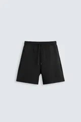 Bermuda negra relaxed fit confeccionada en tejido interlock de algodón con elasticidad. Cintura elástica ajustable con cordón. Bolsillos laterales y detalle de bolsillo trasero de plastrón.